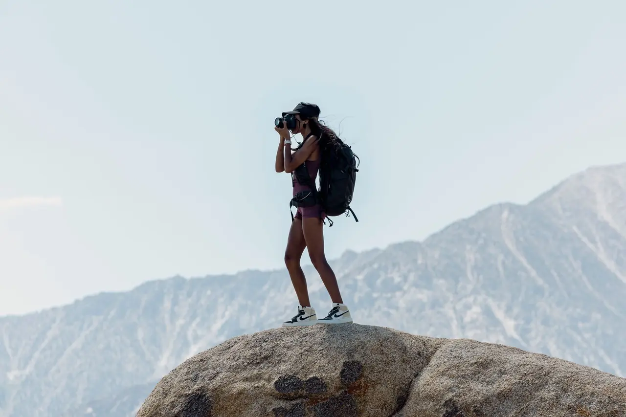 Backpacker standing on a granite boulder photographing the view with a camera, mountains in the background