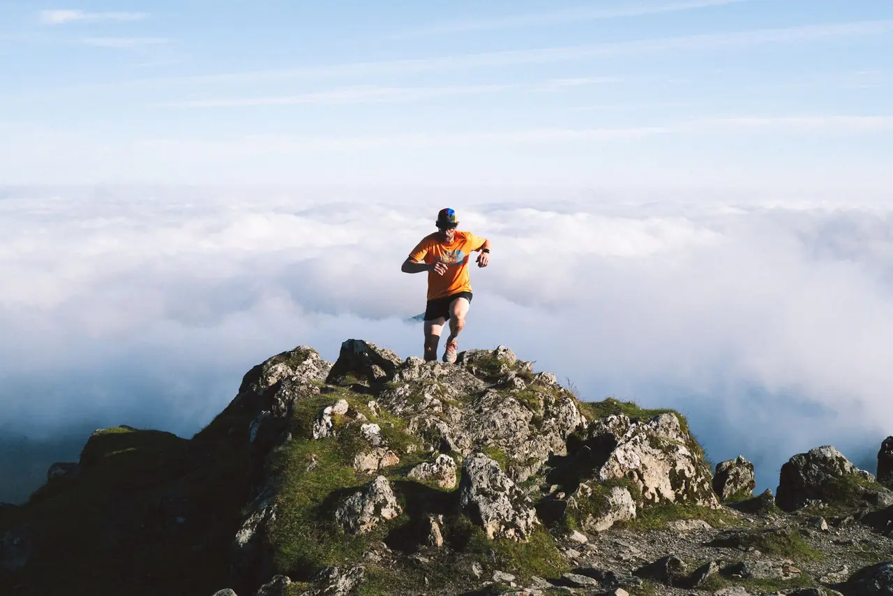 Hiker moving across an exposed rocky summit outcrop high above a sea of clouds