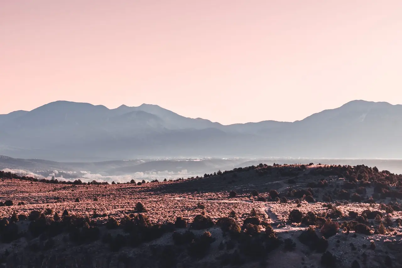 Desert scrubland and juniper-dotted hills below hazy mountain ridges at sunrise in the Big Bend region of West Texas