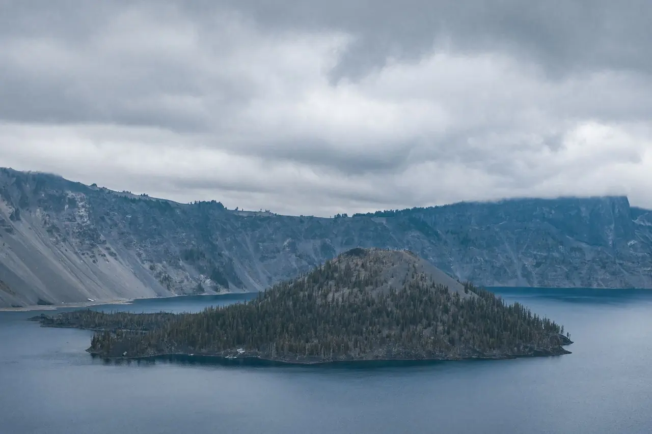Wizard Island rising from the deep blue water of Crater Lake beneath the caldera walls and low clouds