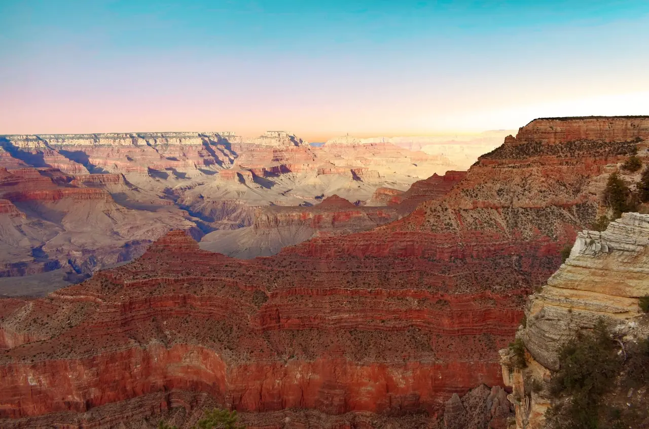 Layered red and tan rock walls of the Grand Canyon seen from the rim under a pastel evening sky