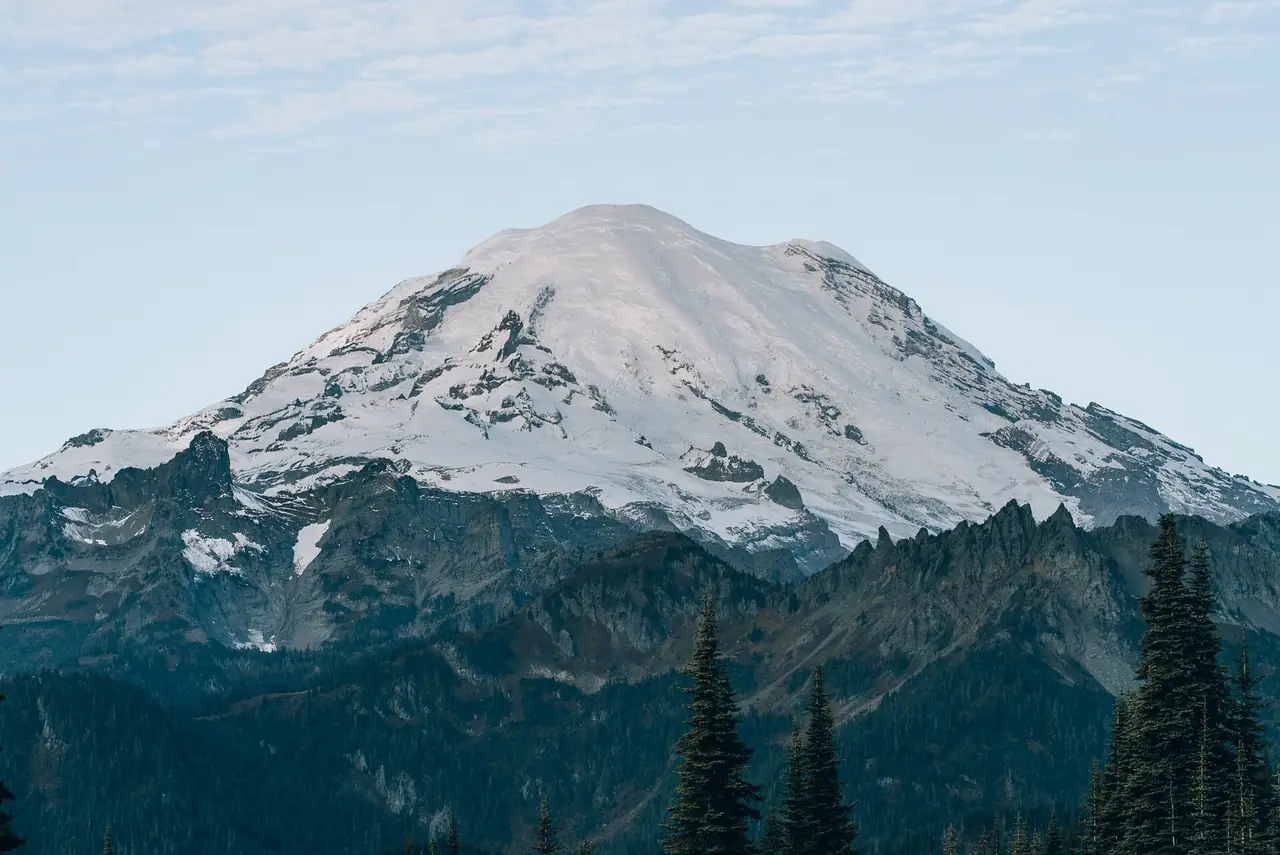 The glaciated summit of Mount Rainier towering above jagged forested ridges, Mount Rainier National Park