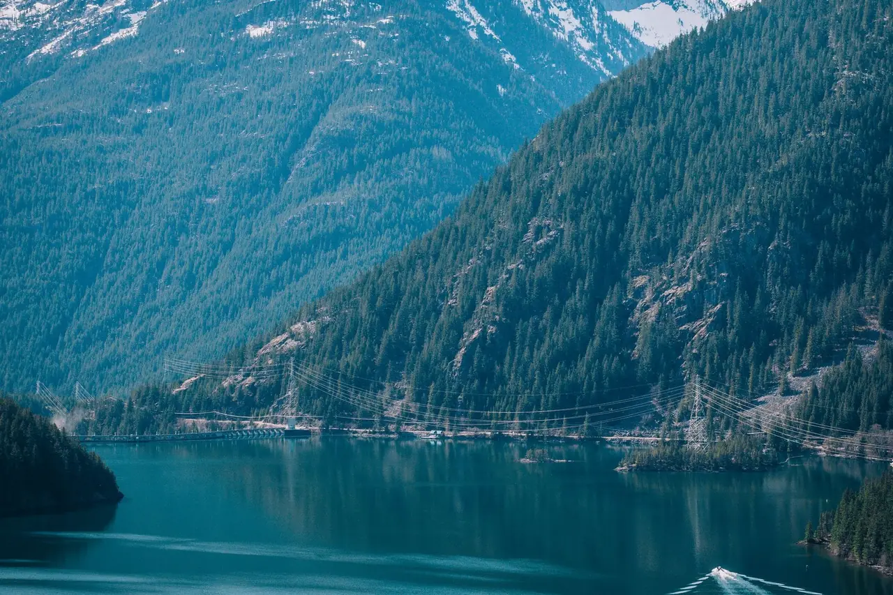 Turquoise Diablo Lake below steep forested slopes and a snow-streaked peak in the North Cascades