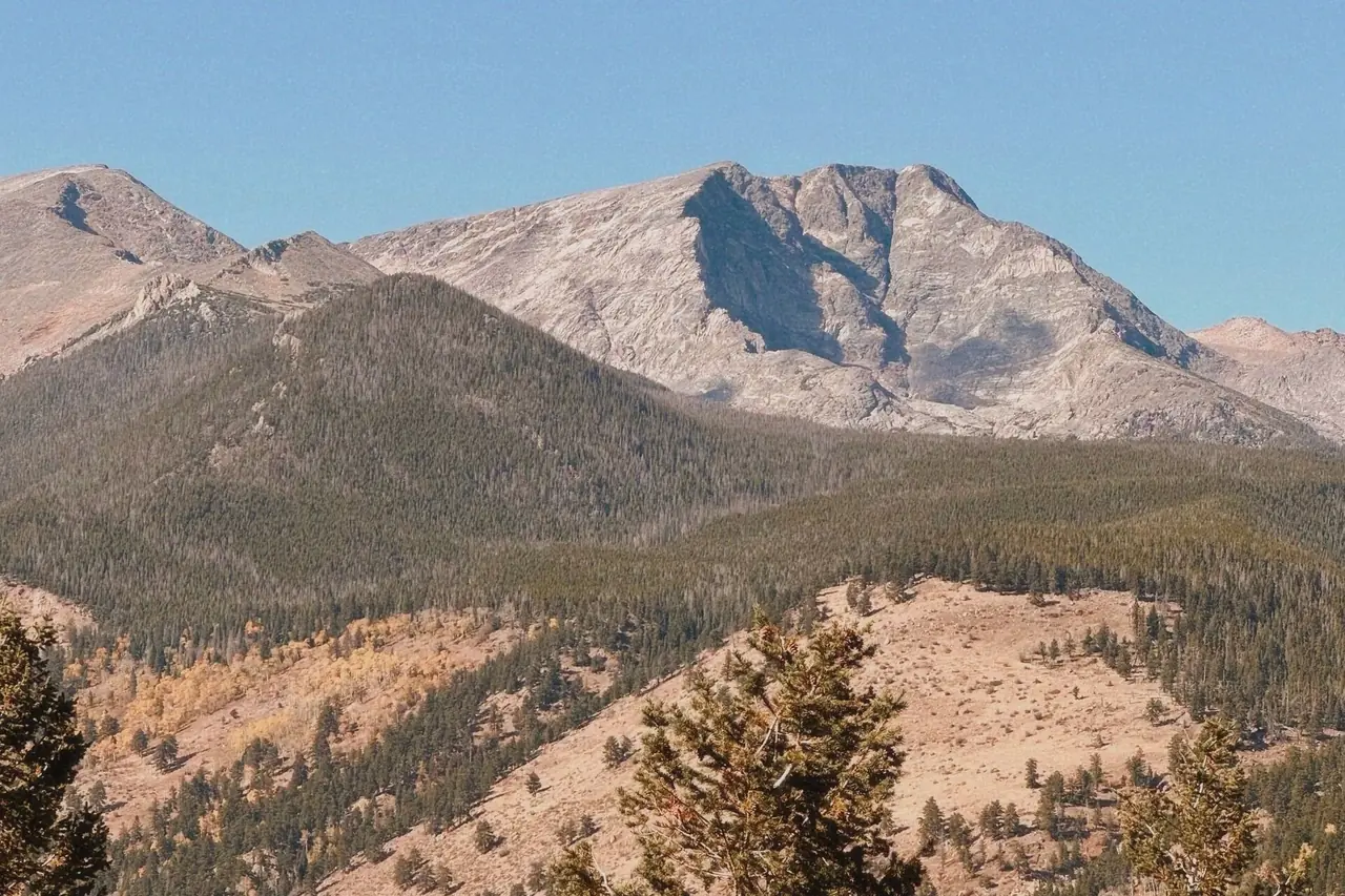Ypsilon Mountain's granite face rising above pine-covered slopes and autumn aspens in Rocky Mountain National Park